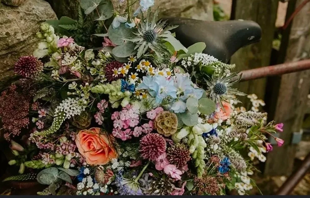 A colorful bouquet of various flowers including roses, daisies, and other wildflowers arranged on a bicycle seat.