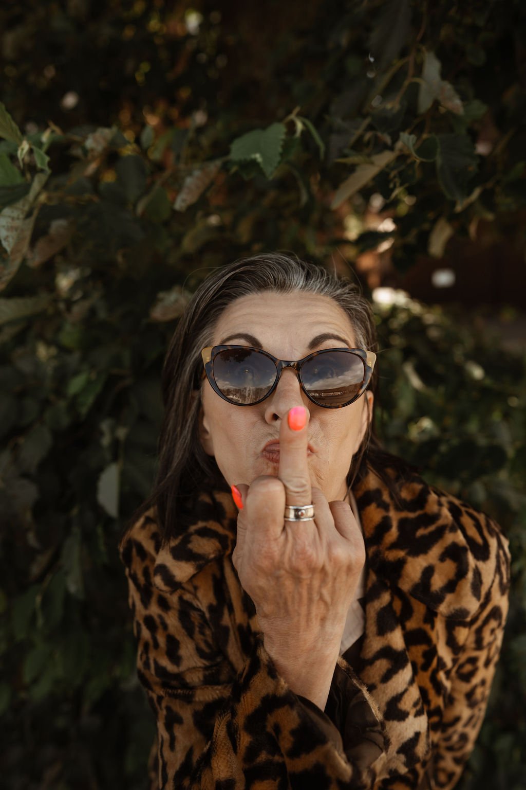 An older woman wearing leopard print coat and sunglasses, making a rude gesture with her middle finger.