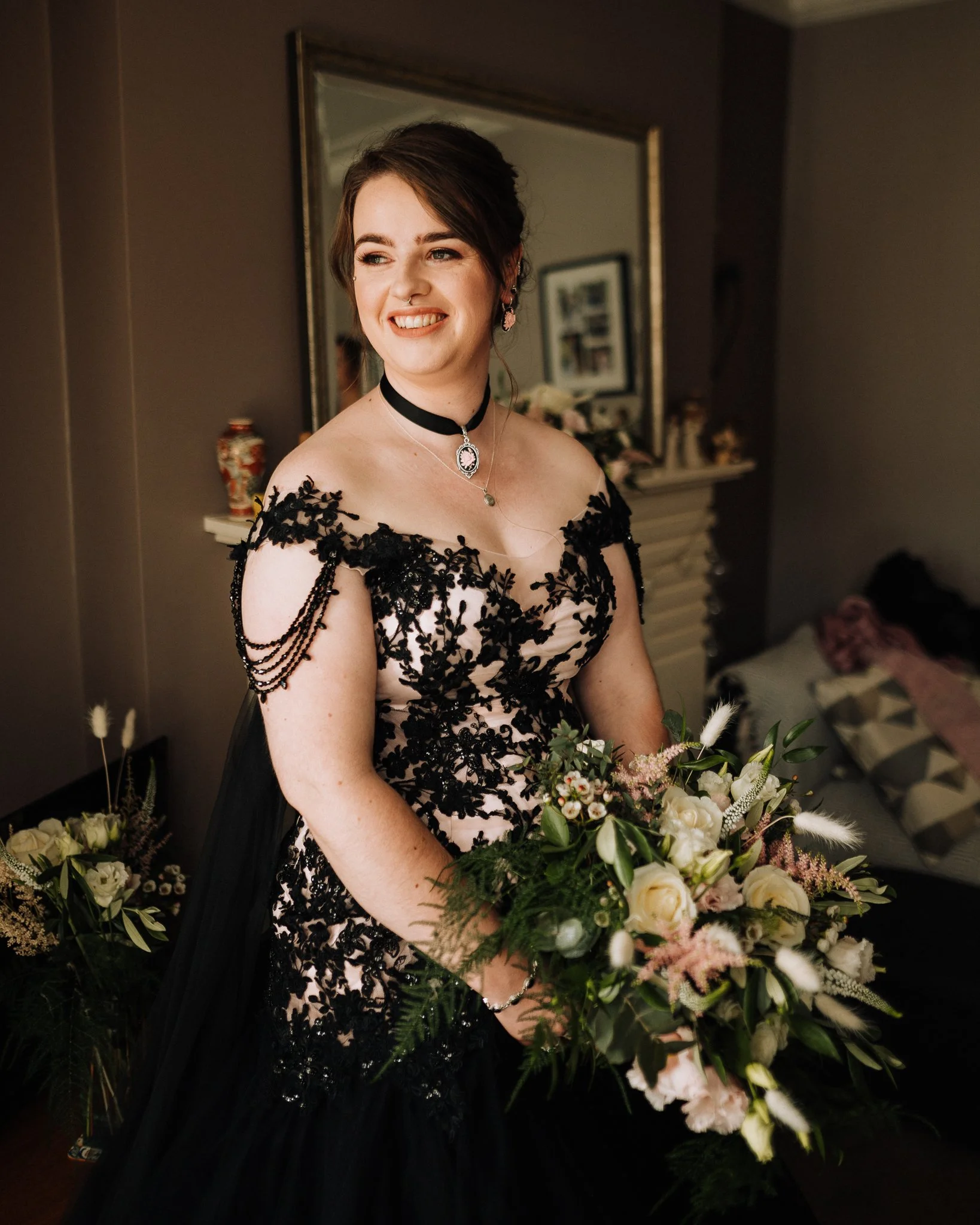 A woman in a black lace dress holding a bouquet of flowers in a warmly lit room.