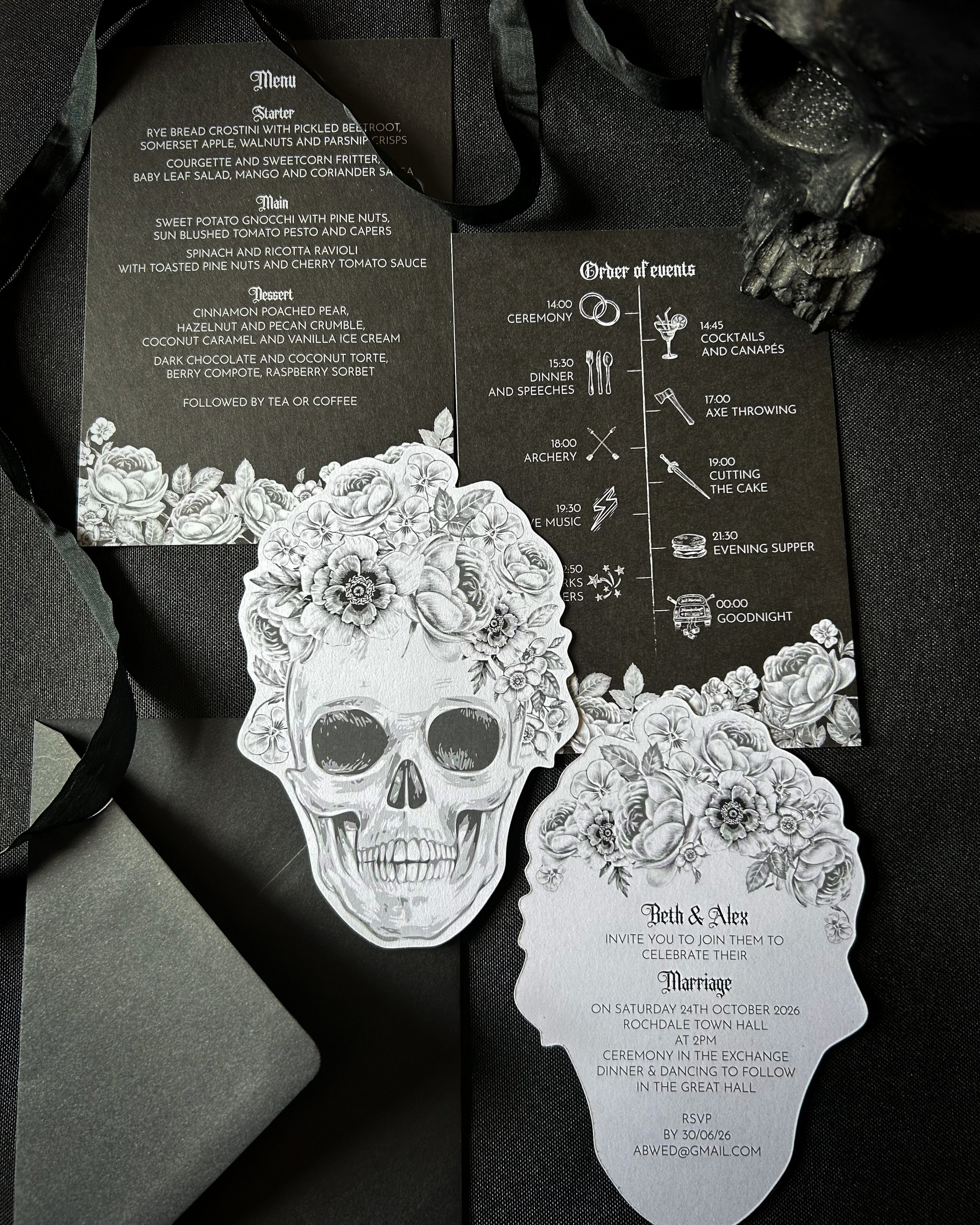 A wedding invitation with black and white floral and skull illustrations, including a detailed schedule of wedding events and a separate wedding RSVP card with floral design.