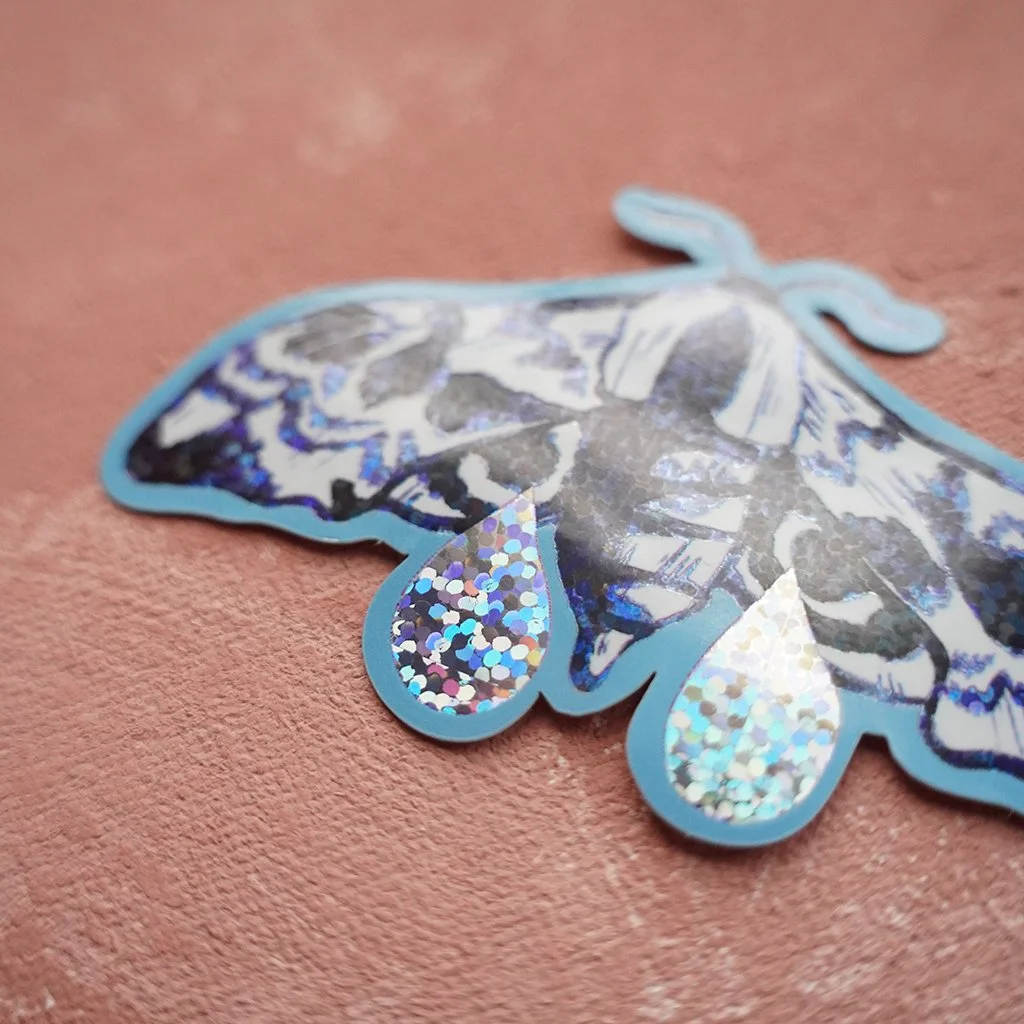 Kiiltävä tarra, jossa on kuva sinisiipikiitäjästä ja kyyneleistä, holografinen glitter-efekti.