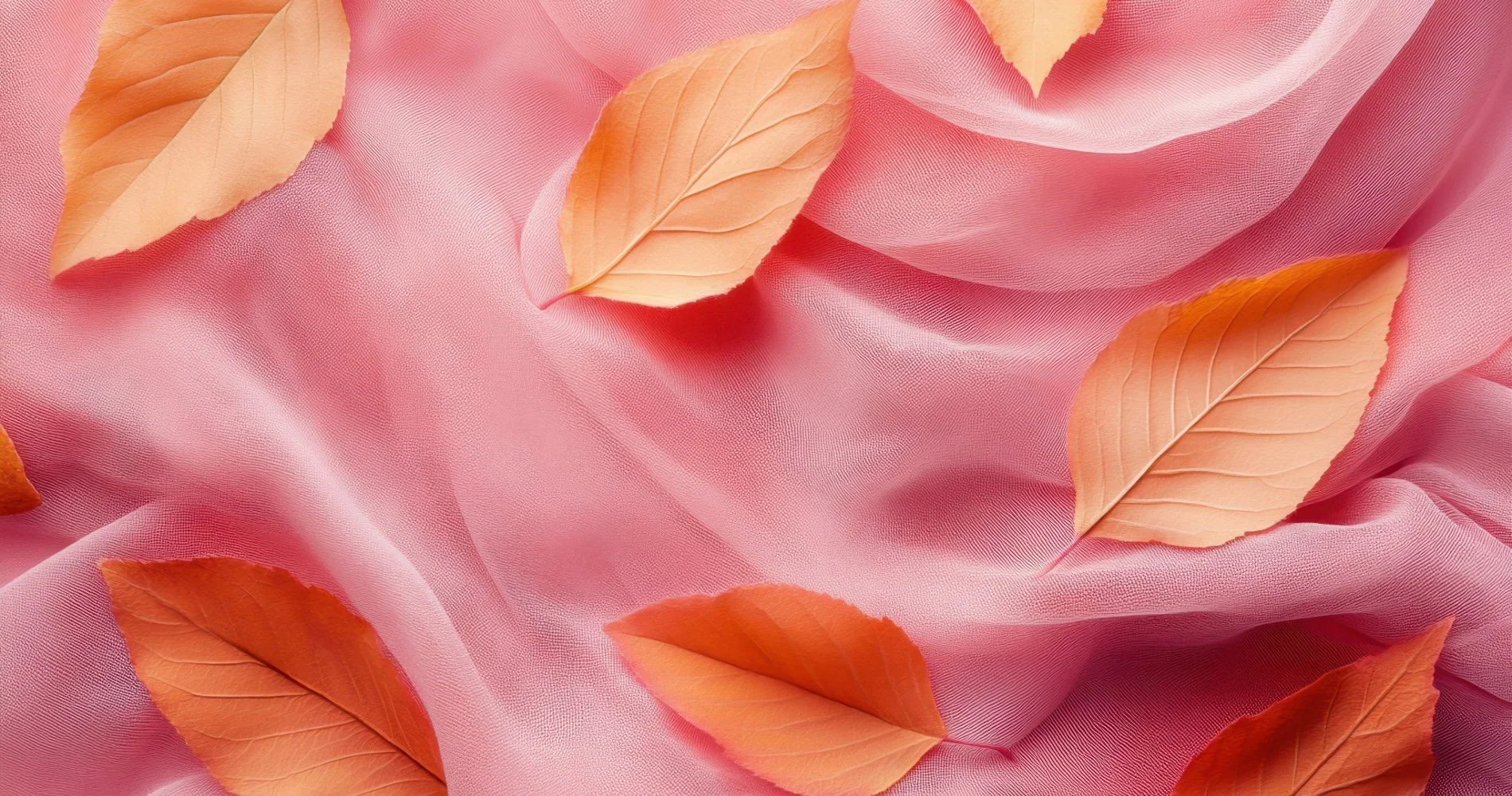 Fallen orange and beige leaves scattered on a soft pink fabric background.
