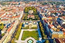 Aerial view of a city park with green lawns, pathways, and surrounding buildings.