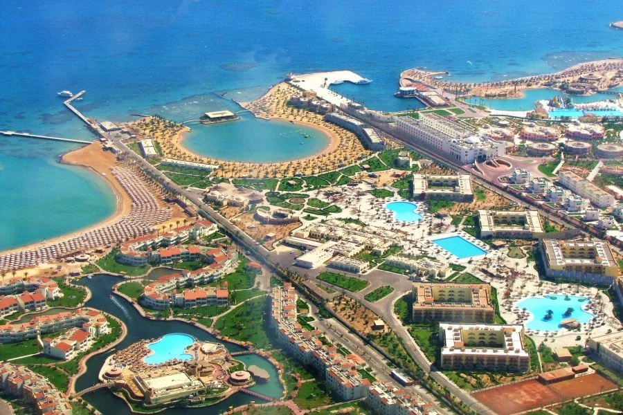 Aerial view of a luxurious beachfront resort with multiple pools, green landscaping, sandy beaches, and oceanfront facilities in Egypt.