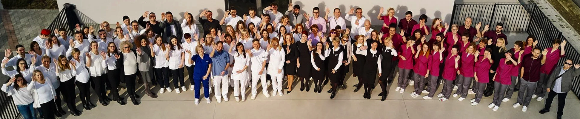 Group photo of diverse healthcare workers and staff from Ars Salutaris Clinic on a rooftop, waving at the camera.