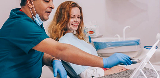 Dr Wael Fekry and a female patient in his dental clinic, he's using a laptop to show the smiling patient their progress.