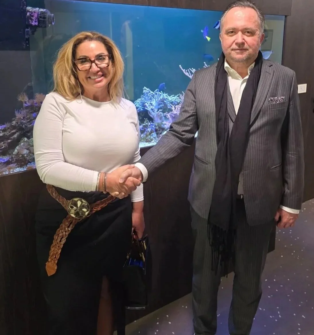 Both owners of TCS and of Clinic in Croatia, woman and man shaking hands in front of an aquarium in the Clinics waiting area, both dressed smart.