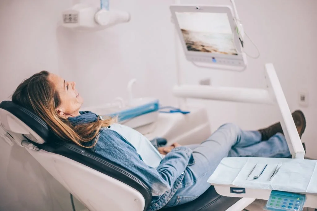 Woman lying in a dental chair with dental tools and a monitor next to her in a dental clinic.