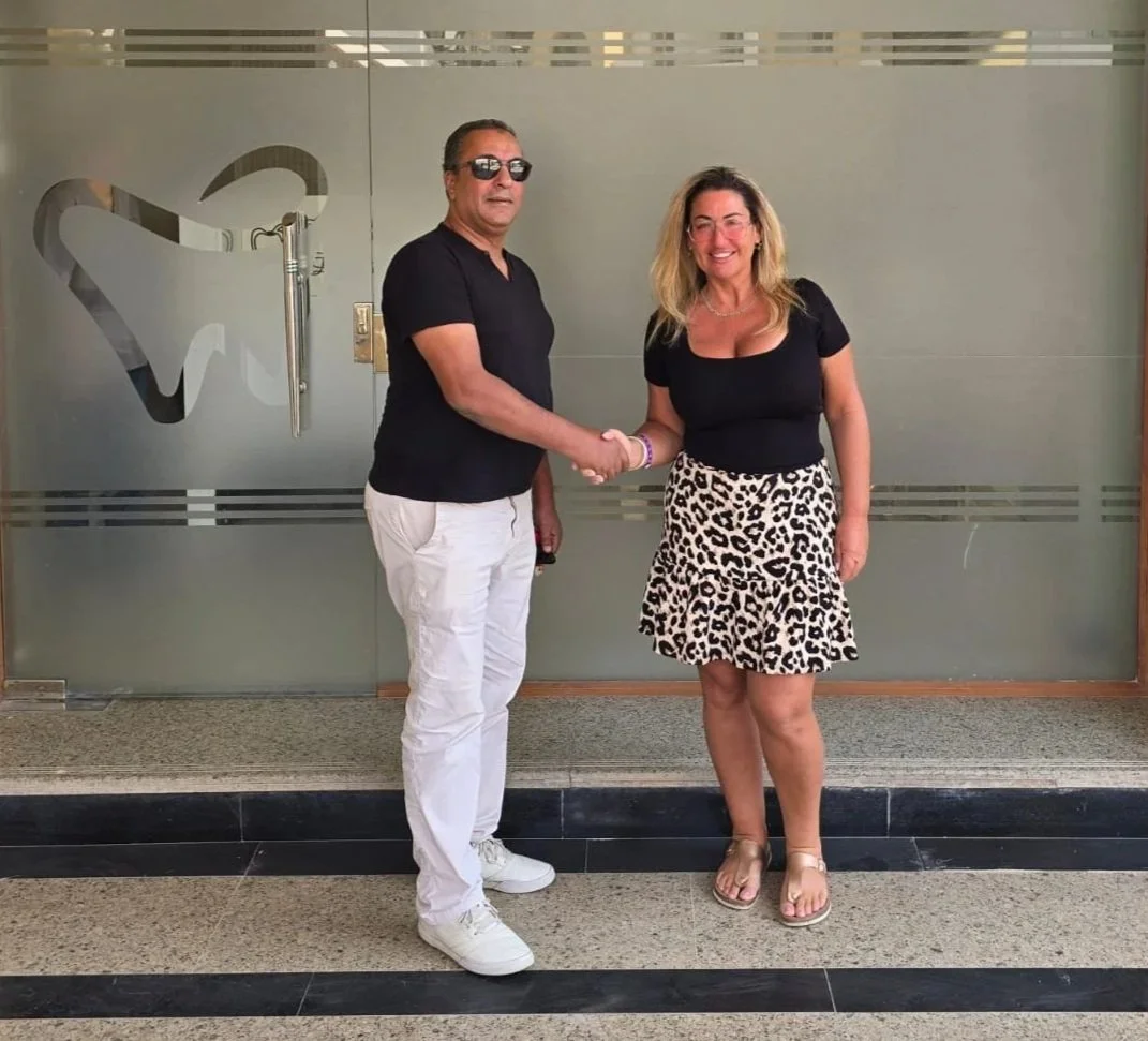 Both owners of TCS and of Clinic in Egypt, man and woman shaking hands outside a dental office with a tooth logo on the door, smiling, dressed casually.