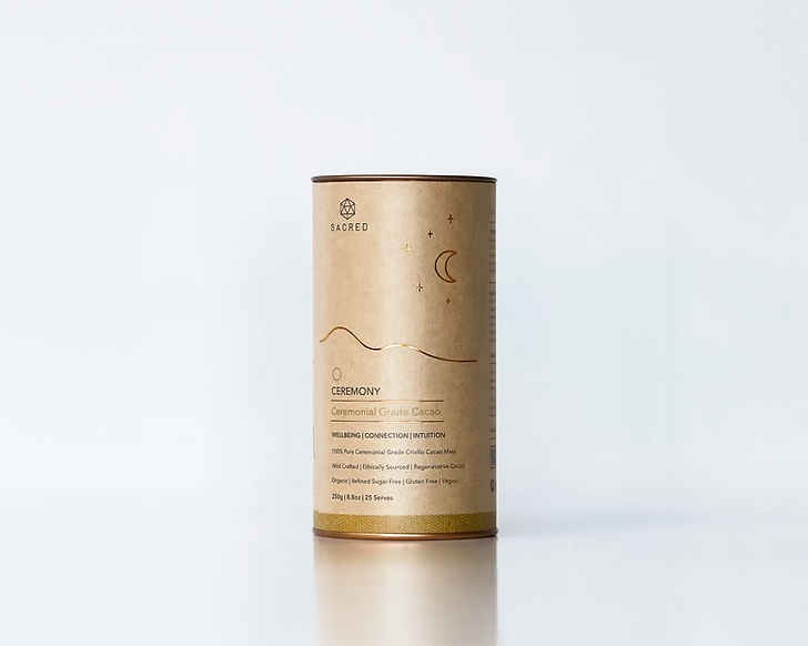 A cylindrical container of Sacred Ceremony ceremonial grade cacao with minimalist design, a black top, and gold accents on a plain light background.