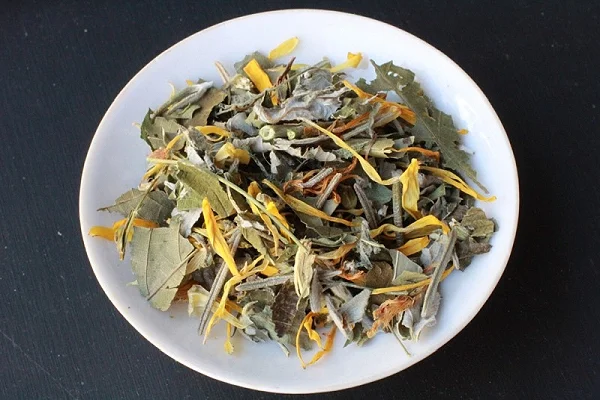 Dried herbal tea leaves with yellow flower petals on a white plate.