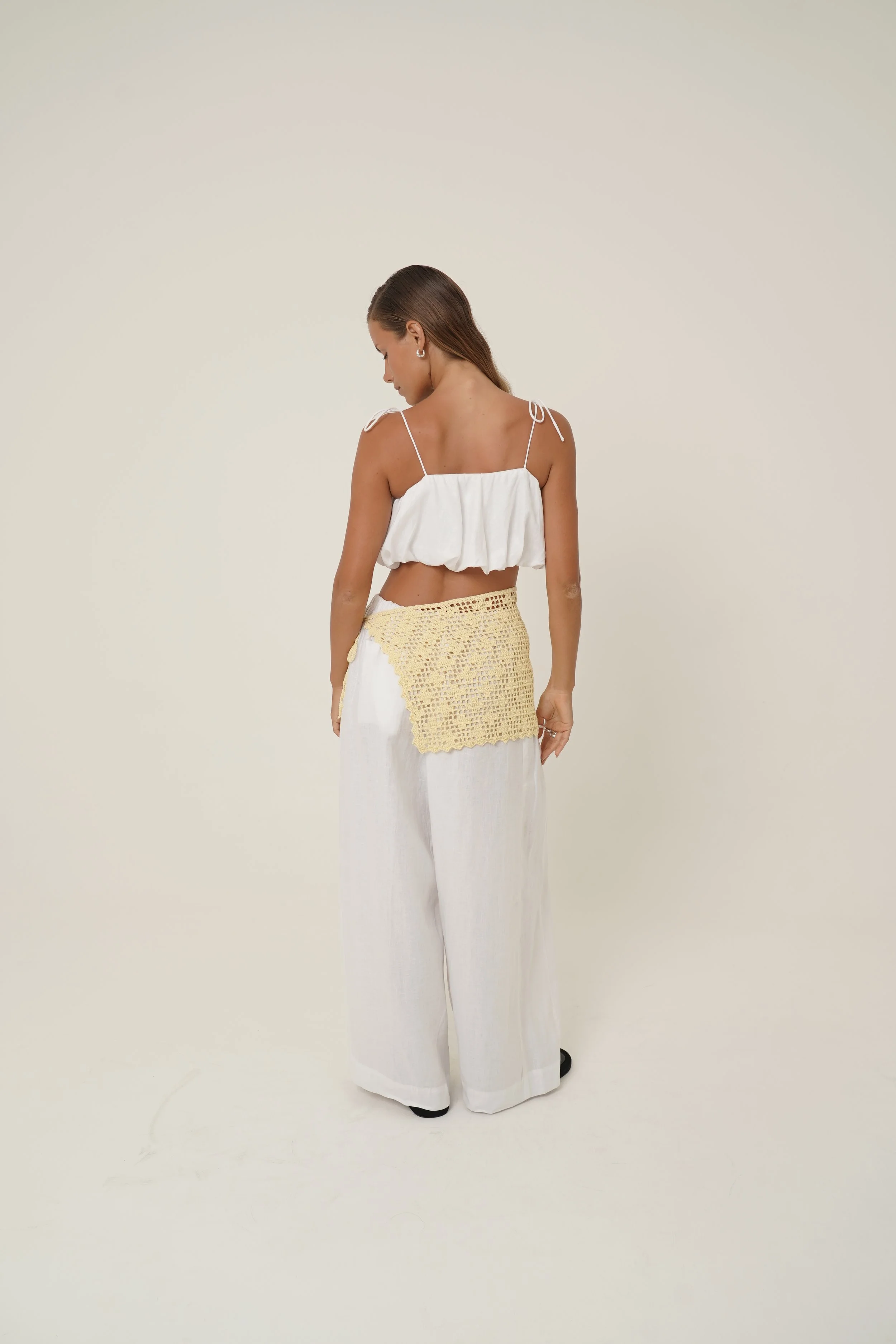 Woman looking down wearing white linen Crescendo Set with Crochet Labelle Sarong
