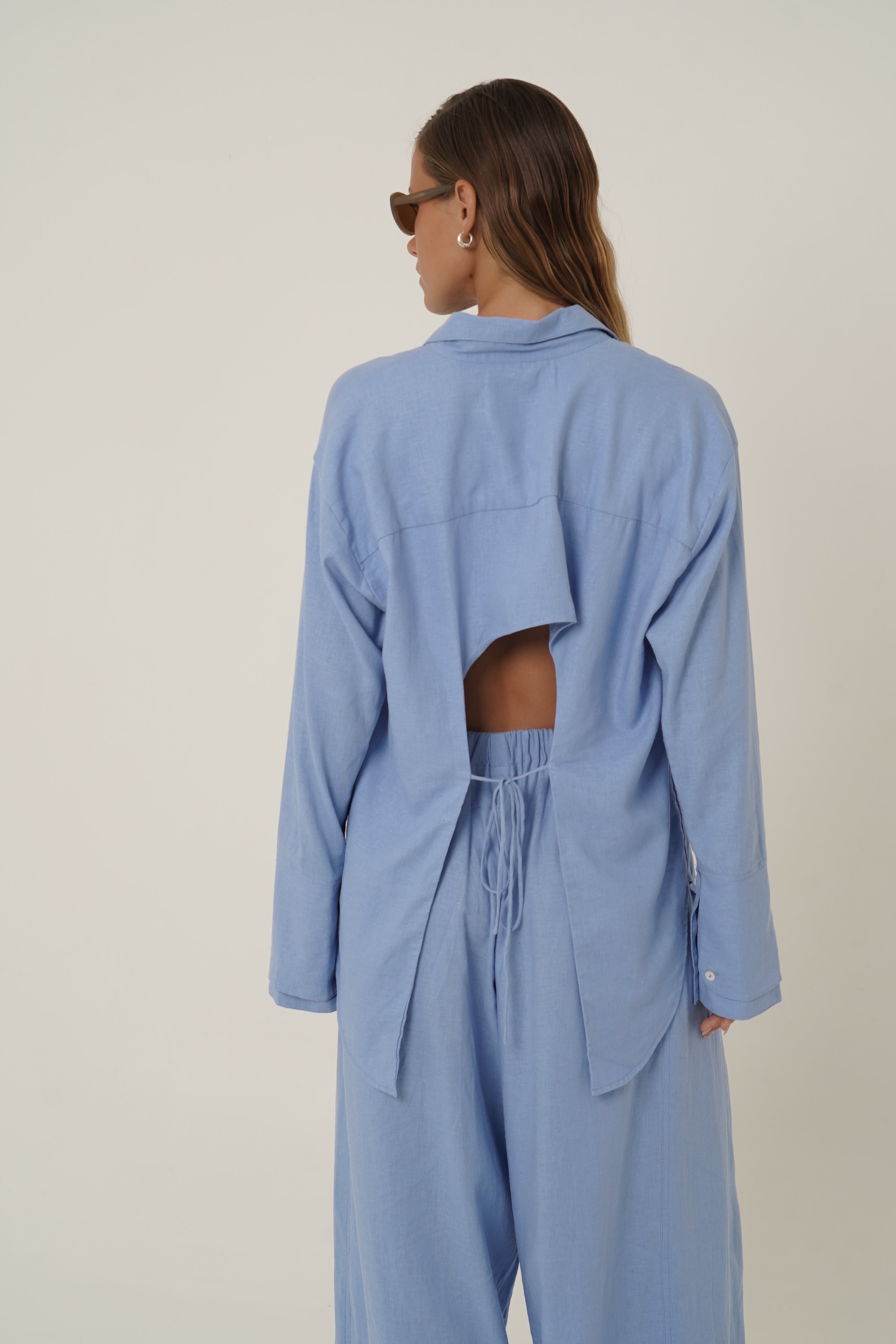 Woman wearing blue Reformation Shirt with open back and sunglasses
