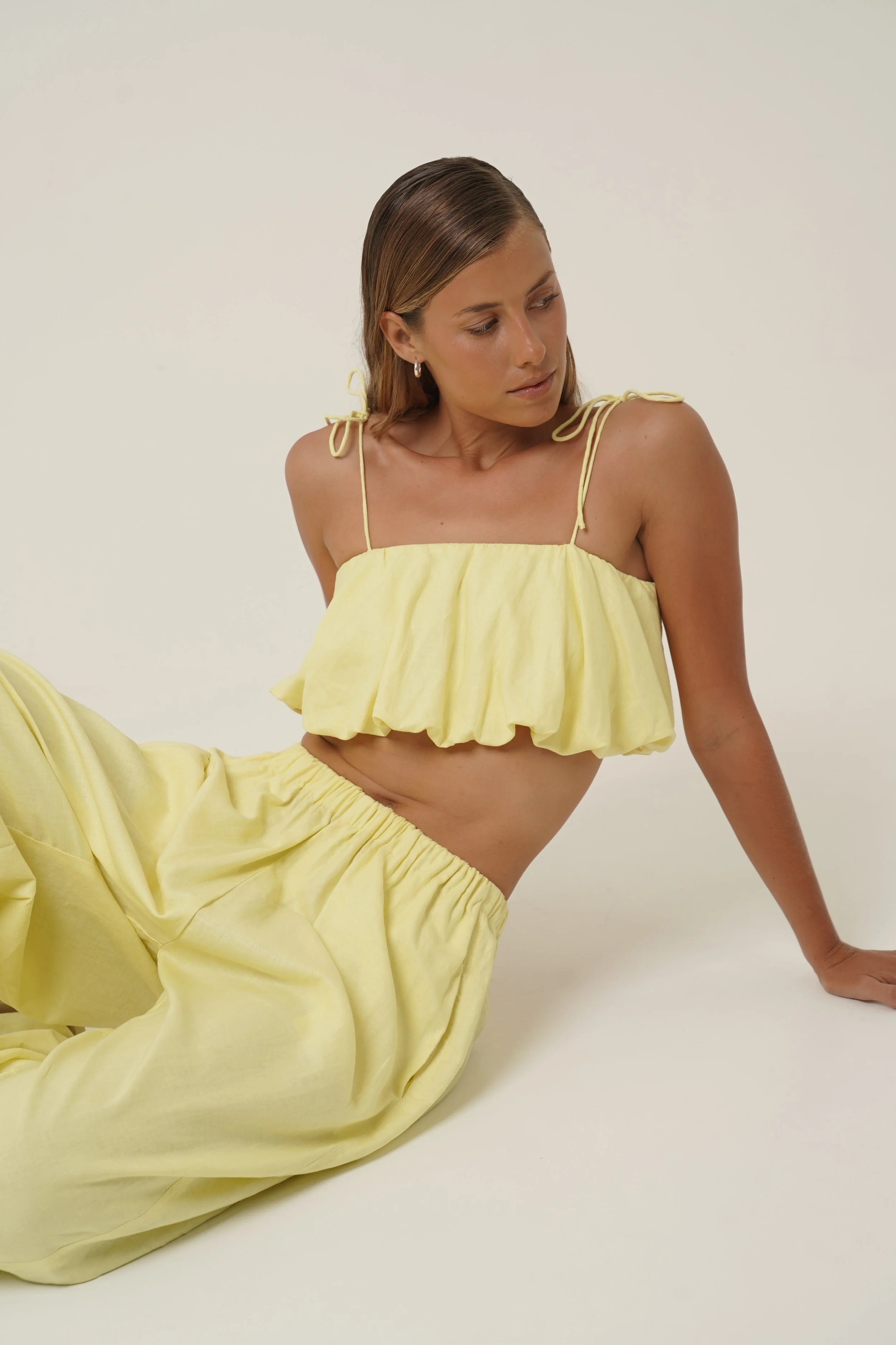 Woman wearing Crescendo Top & Bottoms in lemon colored pure linen sitting down