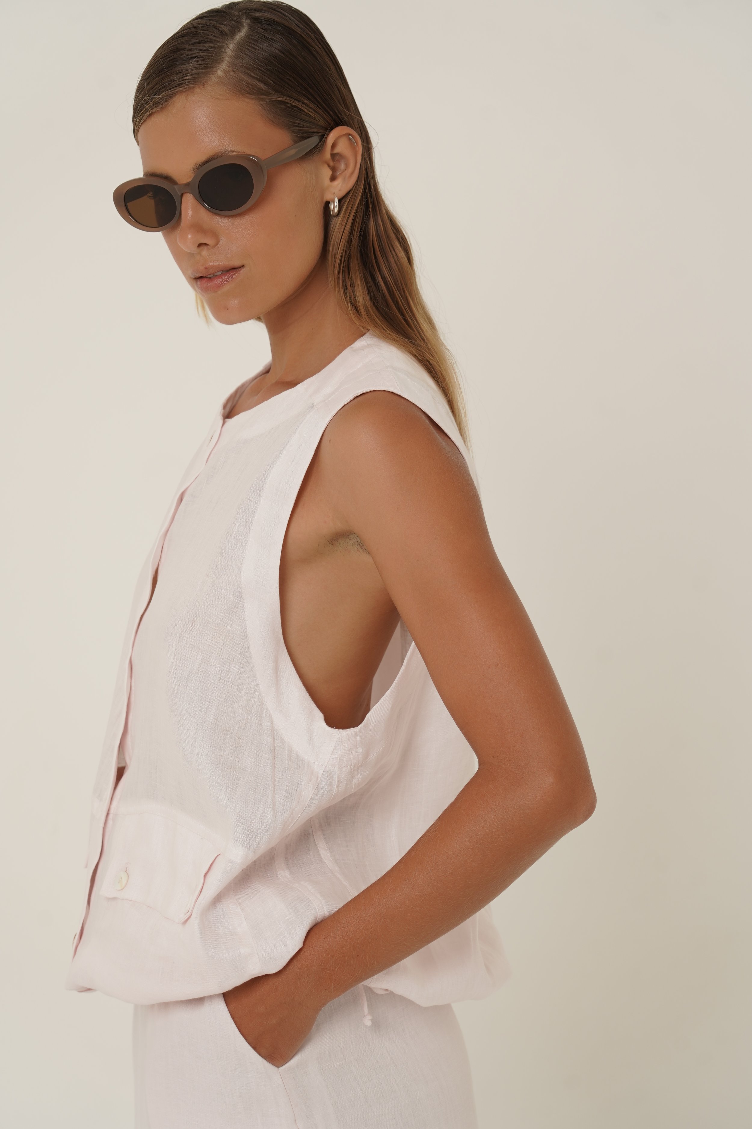 Woman wearing linen Maribou Vest with pockets, button closure and drawstring at hem - side view