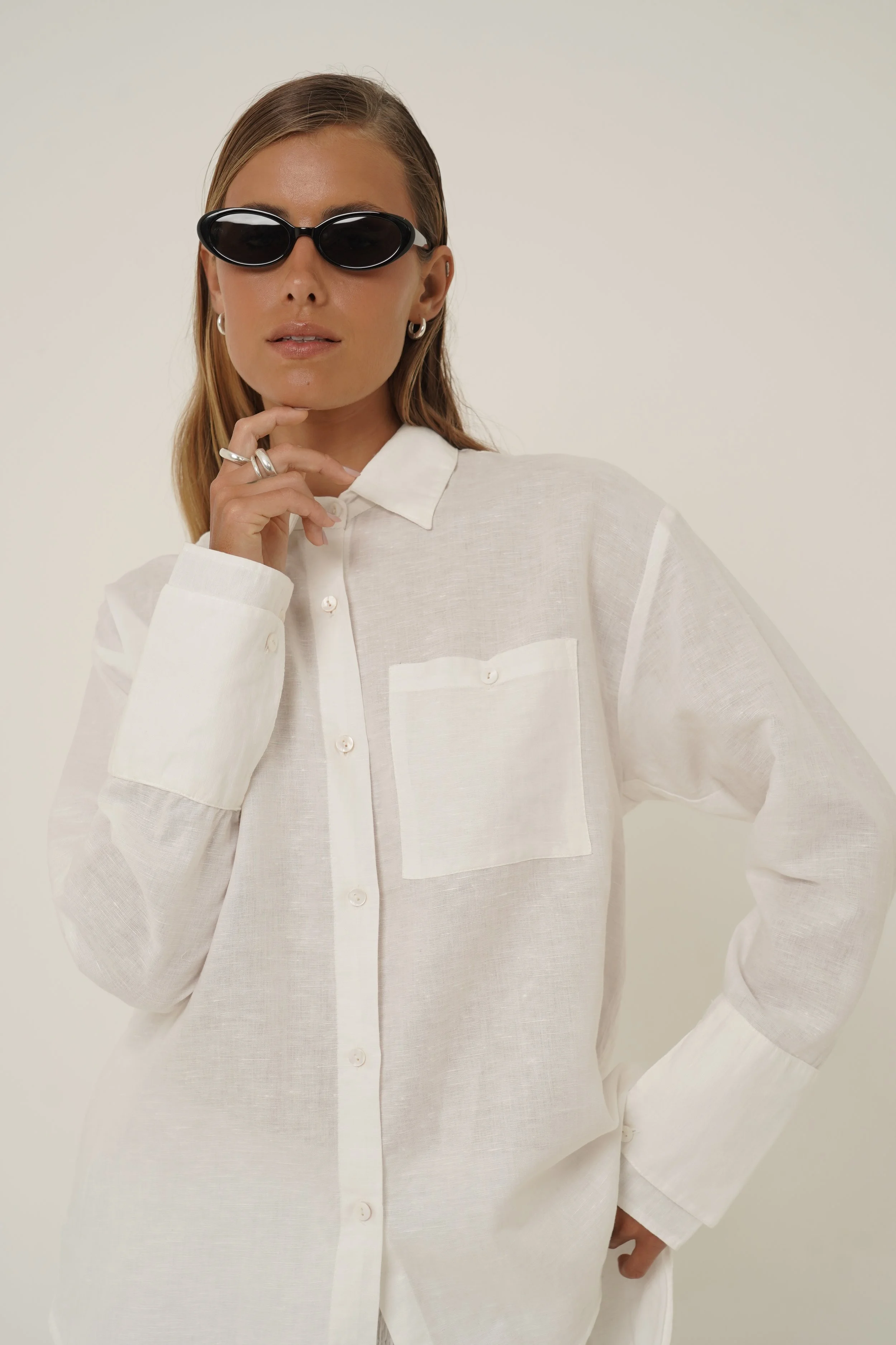 Woman holding her face and wearing white Reformation Shirt in pure linen