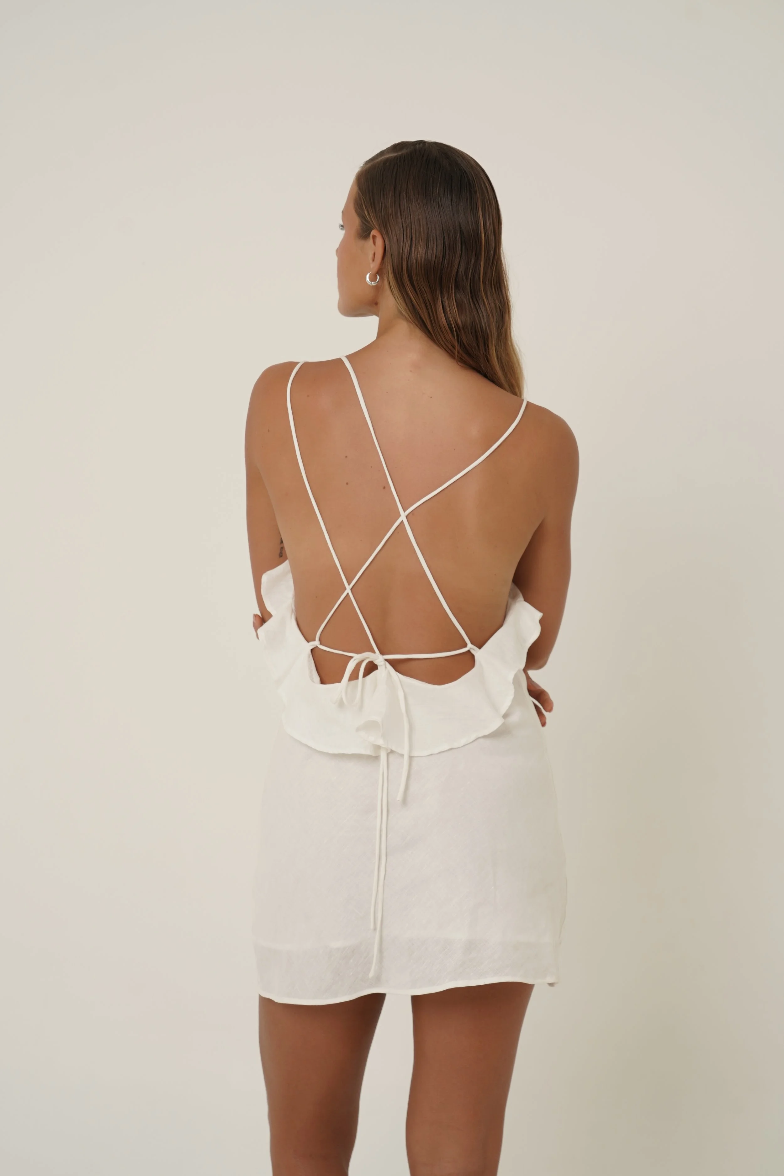Woman wearing Renata Dress in pure white linen with back strap detail  back view