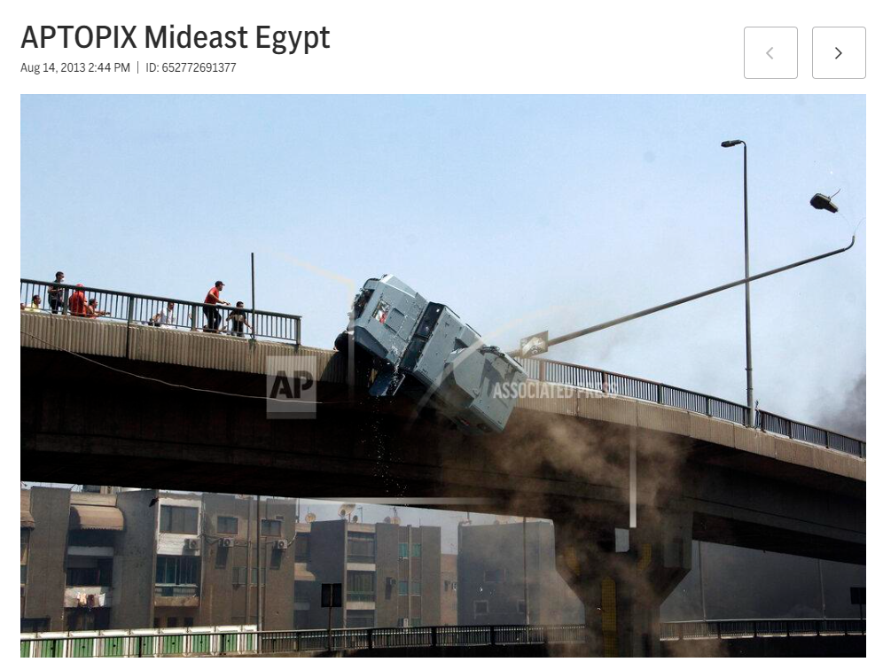 A police car has collided with a street lamp post on a bridge, causing the lamp post to bend and break, with debris falling, while smoke rises below the bridge in a city setting.