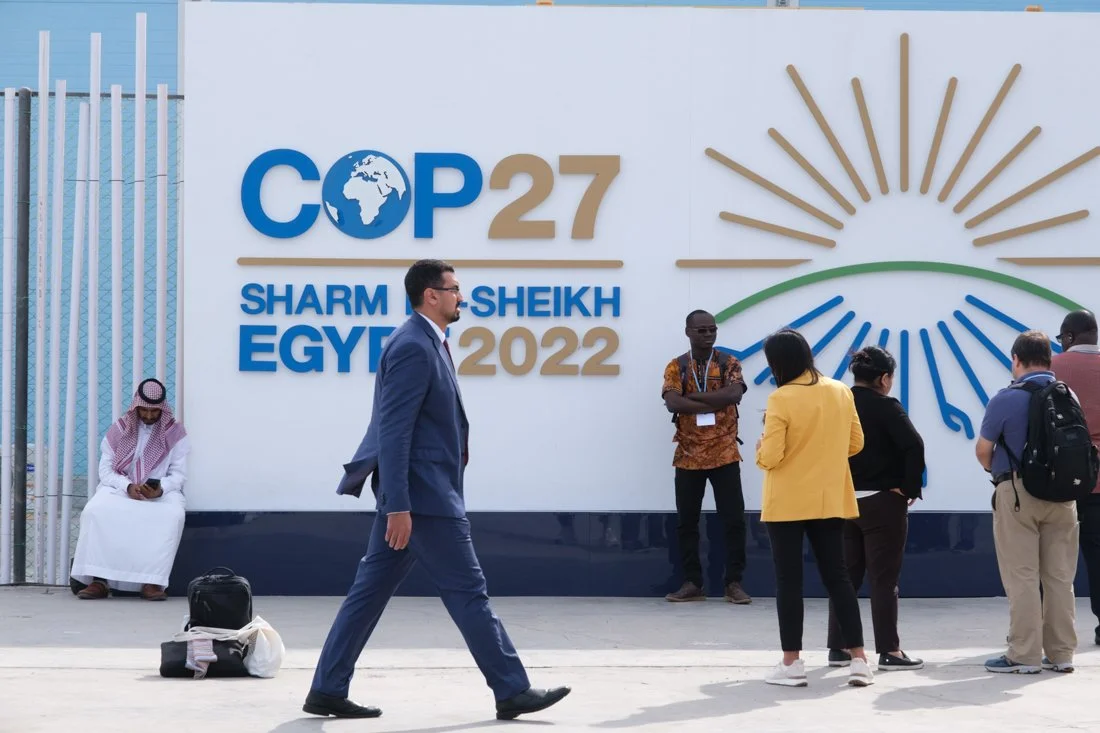 People walking and standing in front of a large sign for COP27 at Sharm El-Sheikh Egypt in 2022.
