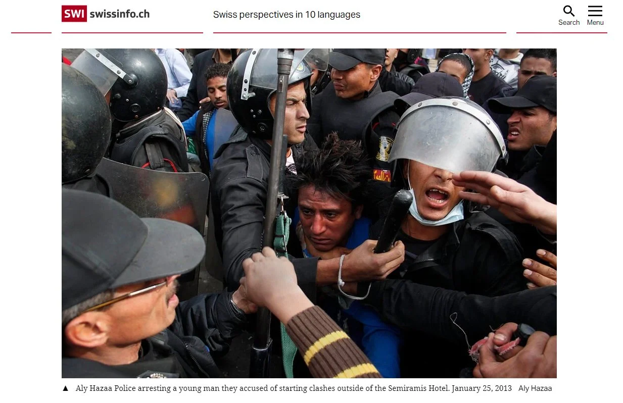 Police arresting a young man in a crowd, with officers wearing helmets, during a protest outside the Semiramis Hotel in 2013.