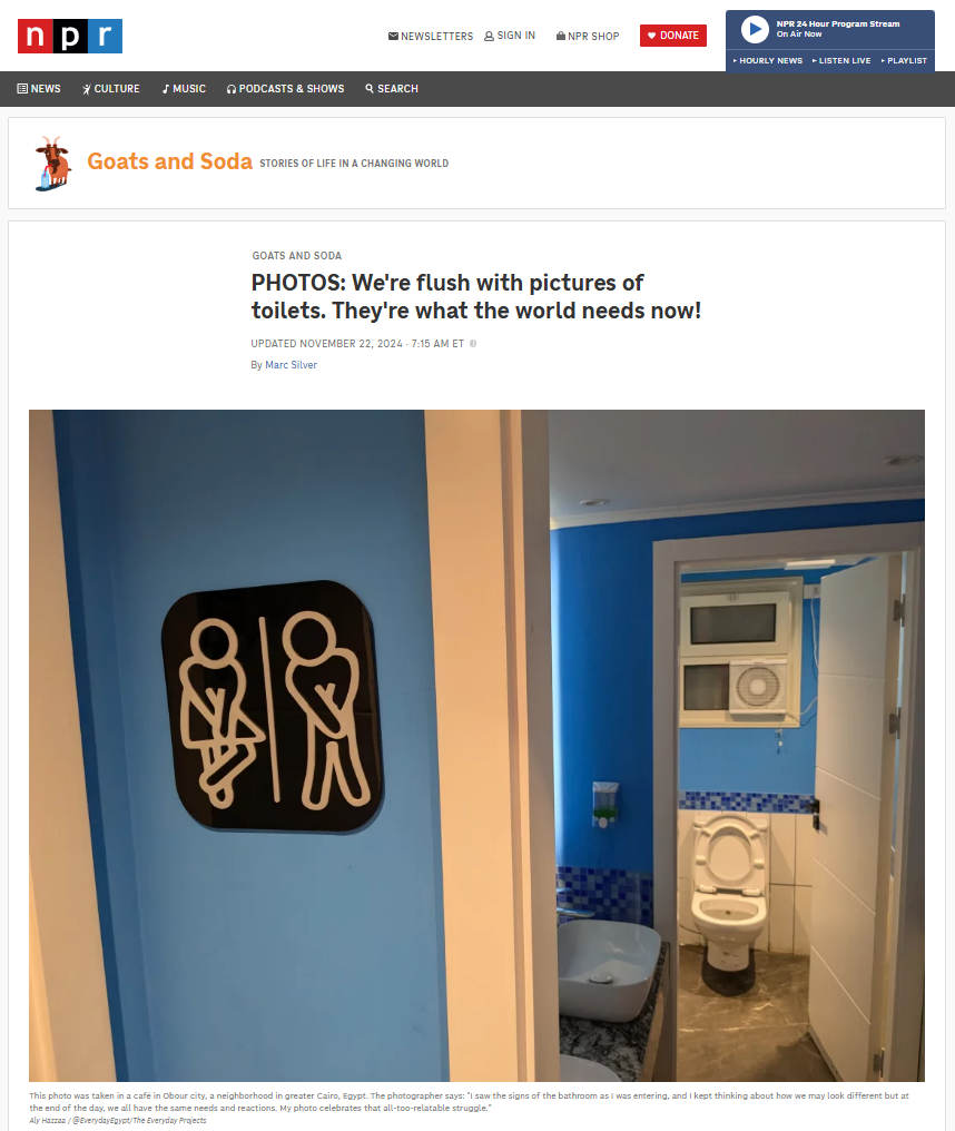 Sign showing male and female restroom symbols on a blue wall, with a small bathroom visible in the background featuring a toilet, sink.