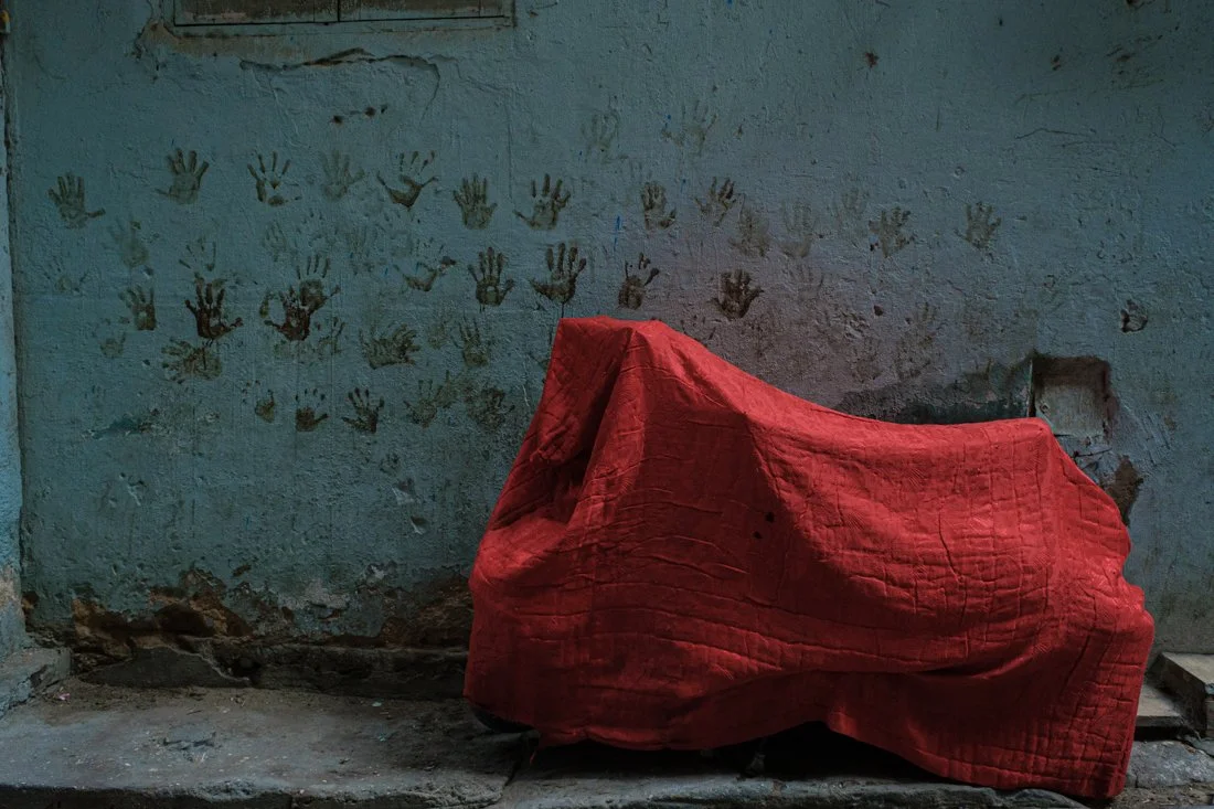 A red cloth covering an object against a wall with handprints painted on it.