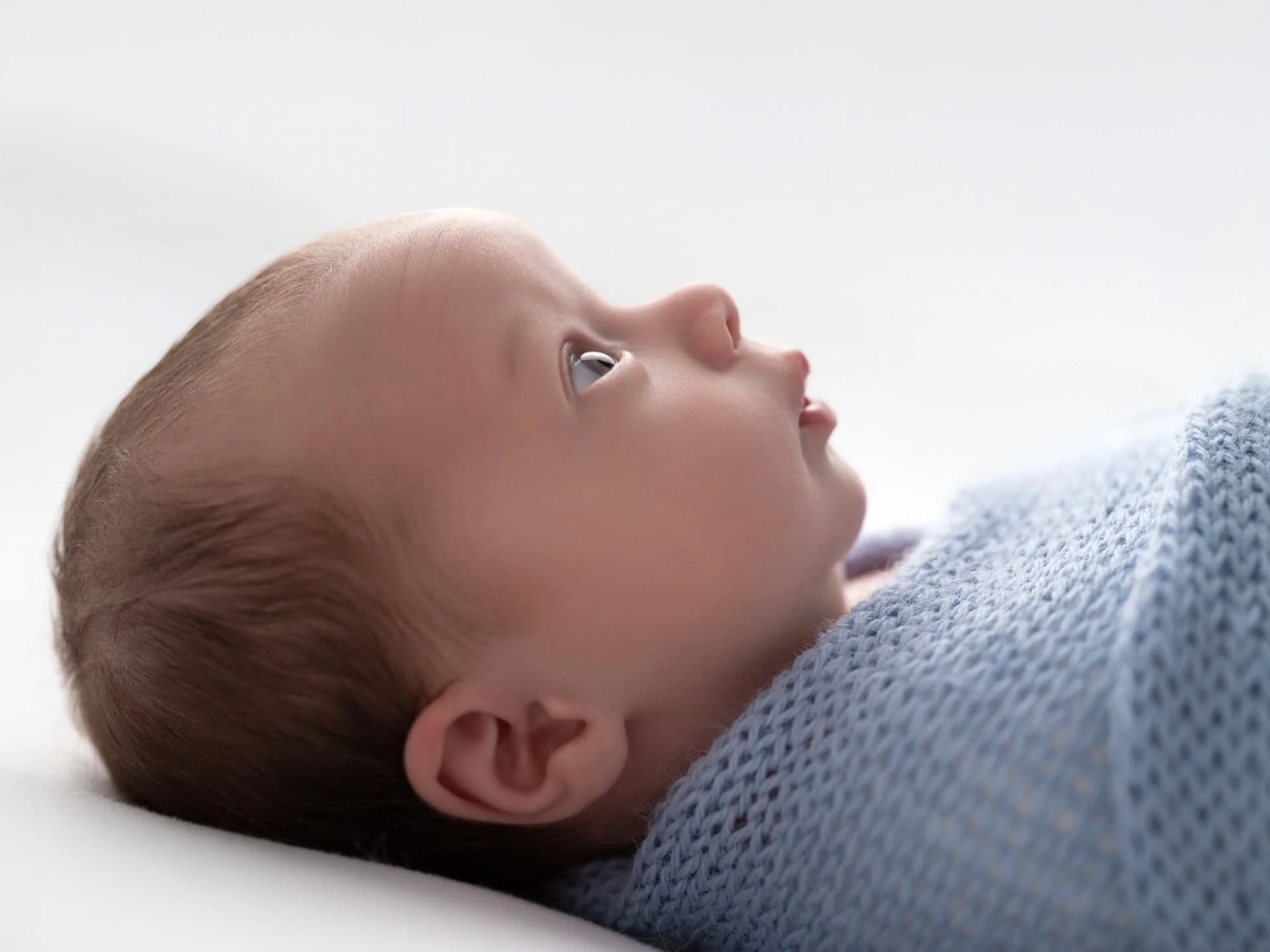 A baby laying on it's back wrapped in a blanket looking up