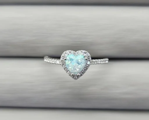 Heart-shaped opal surrounded by small diamonds in a silver ring.