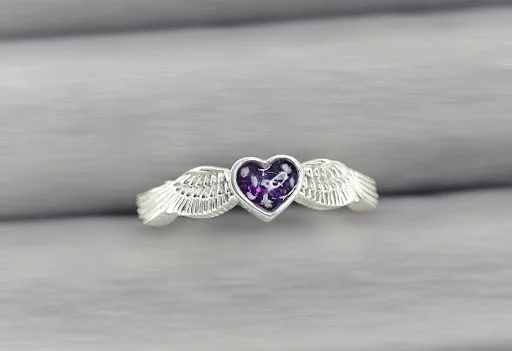Silver ring with a purple heart-shaped gemstone and wing designs on either side.