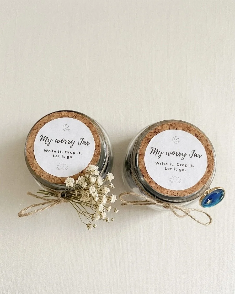 Two glass jars labeled 'My worry Jar' with cork lids, decorated with small flowers and tied twine. The jars contain notes inside.