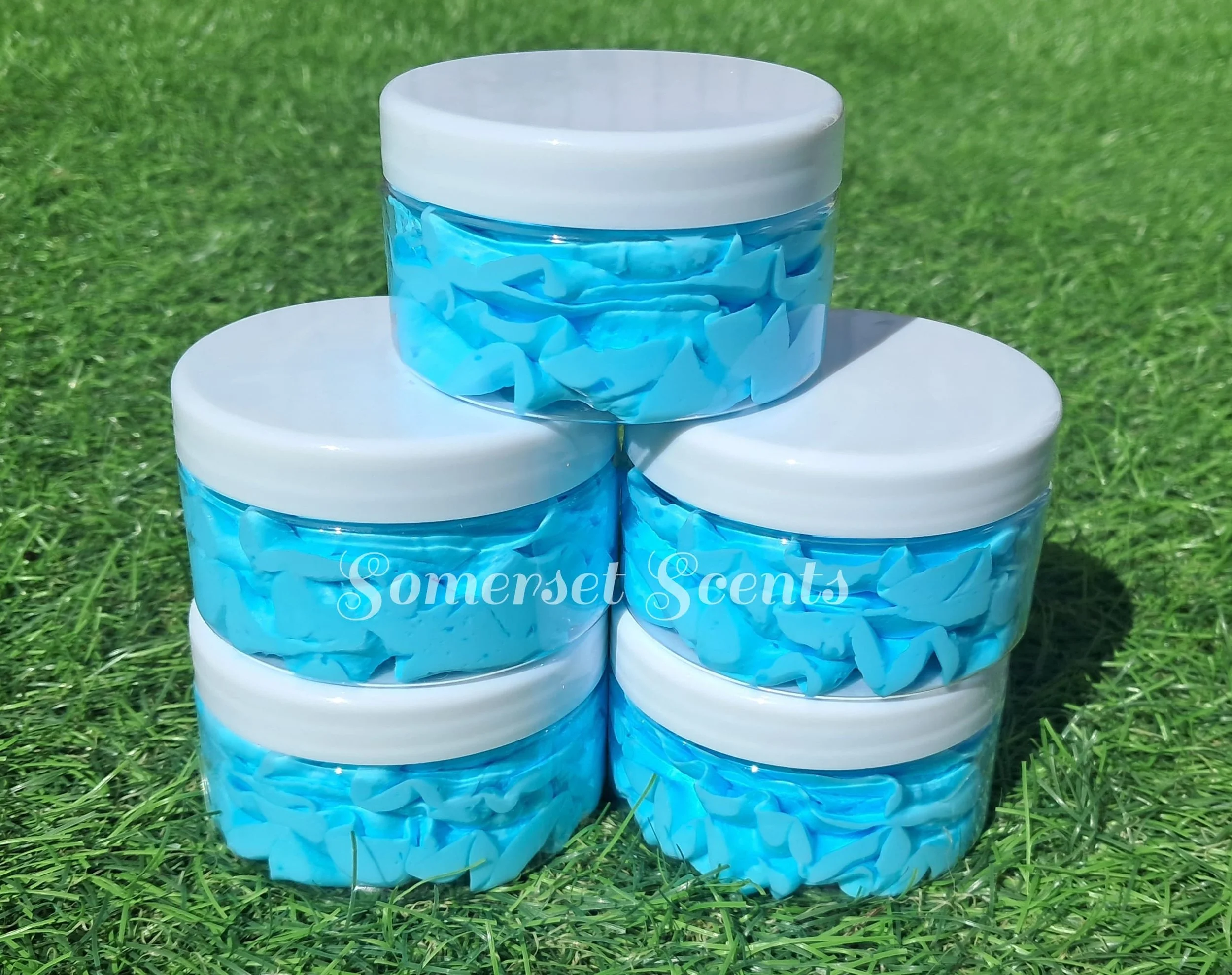 Three white candles with blue ribbon and tissue paper design, placed outdoors on green grass.