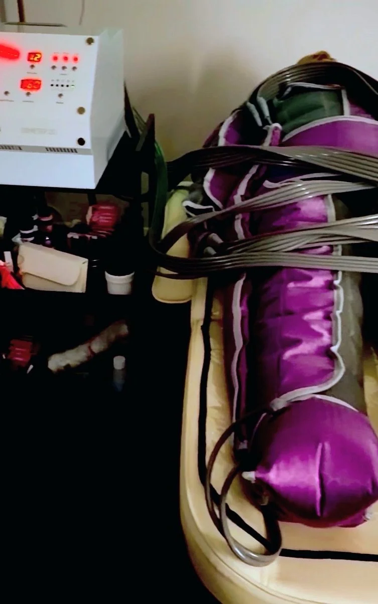 A massage table with a purple and beige blanket and multiple electrical cords on top of it. A machine with red digital readouts is positioned on the left side of the image.