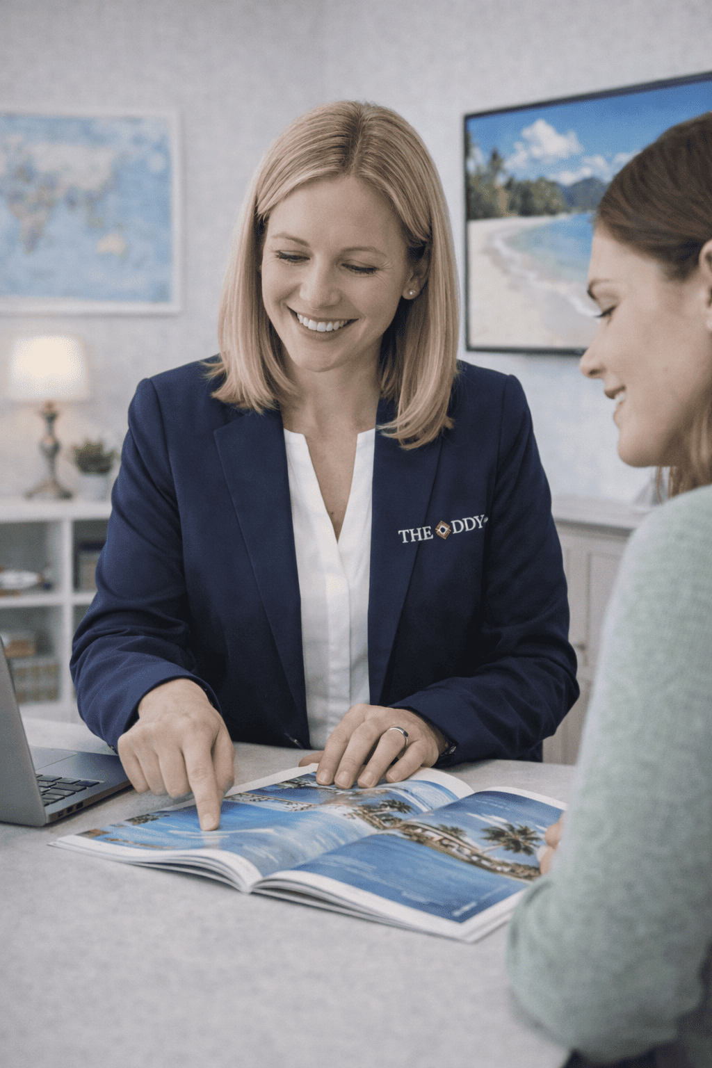 A woman in a blazer pointing to a travel brochure while talking to another woman in an office setting.