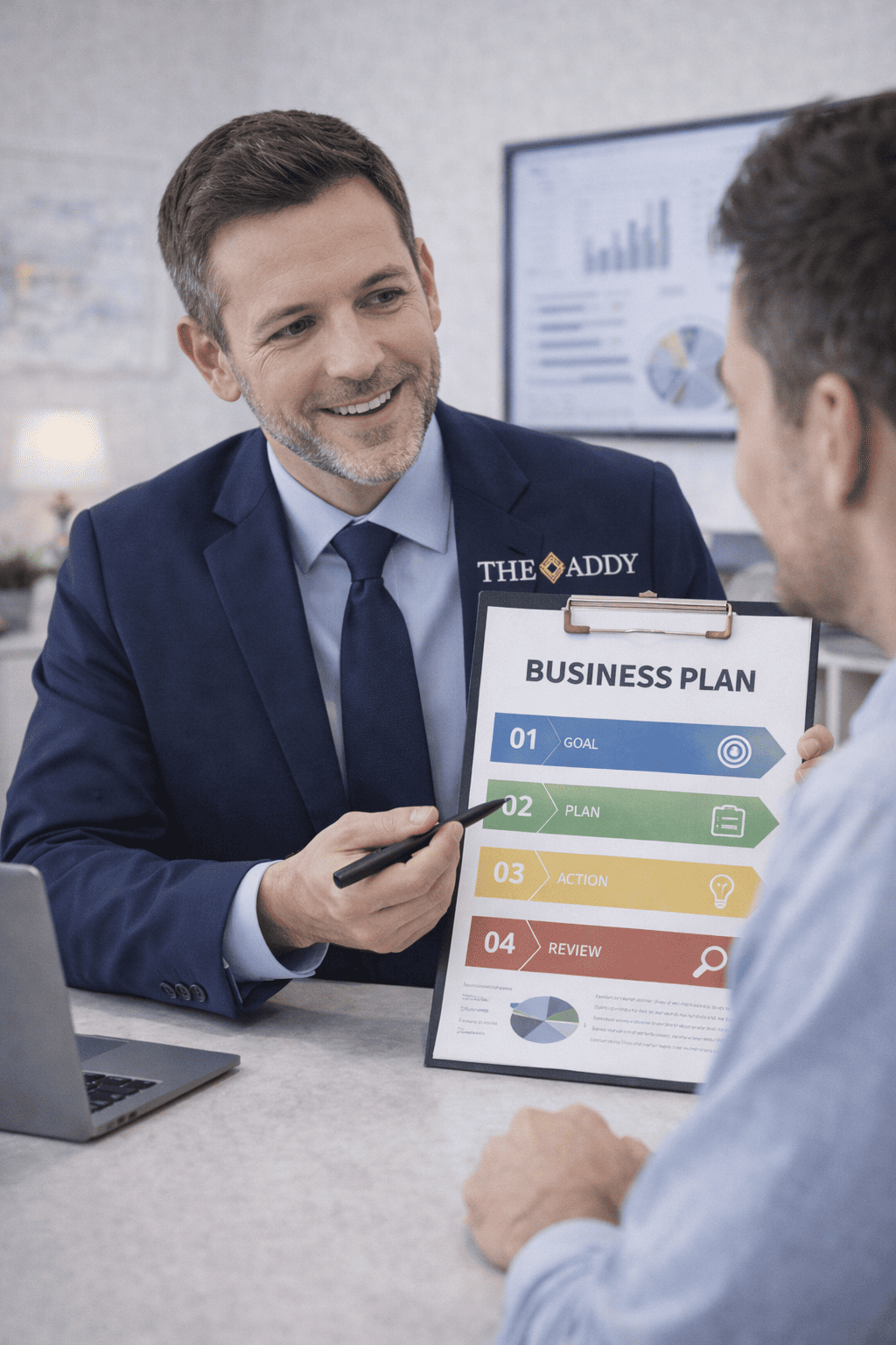 A businessman in a suit and tie smiling and pointing to a business plan on a clipboard, while talking to another man in a white shirt at a desk with a laptop. The business plan lists four steps: goal, plan, action, review.
