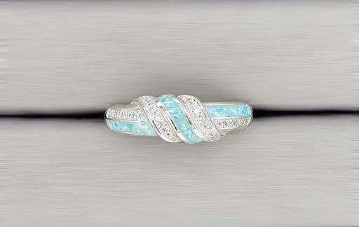 A silver ring with light blue gemstones and small diamonds, designed with a twisted pattern.