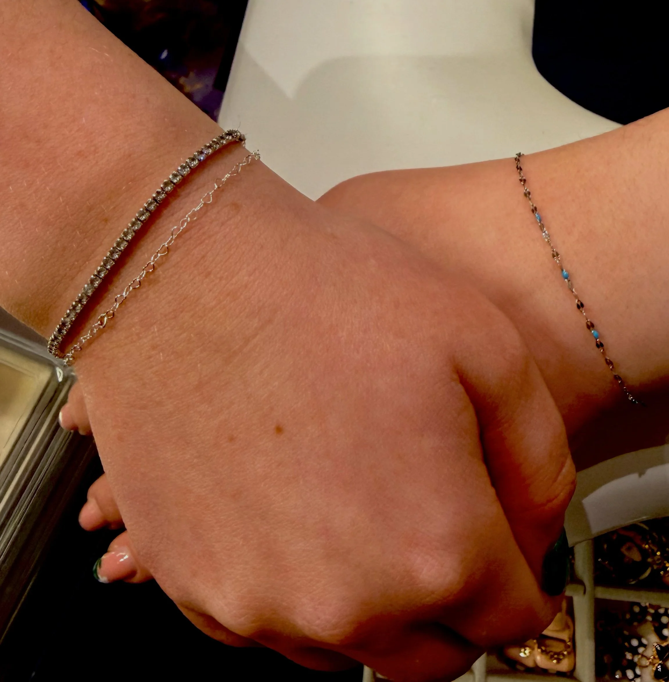Close-up of a person's arm with three bracelets: a diamond-studded bracelet, a delicate silver chain, and a thin bracelet with small beads or stones.
