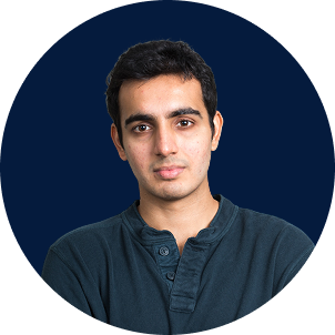 Portrait of a young man with short black hair, wearing a dark blue, long-sleeved shirt, against a deep blue background.