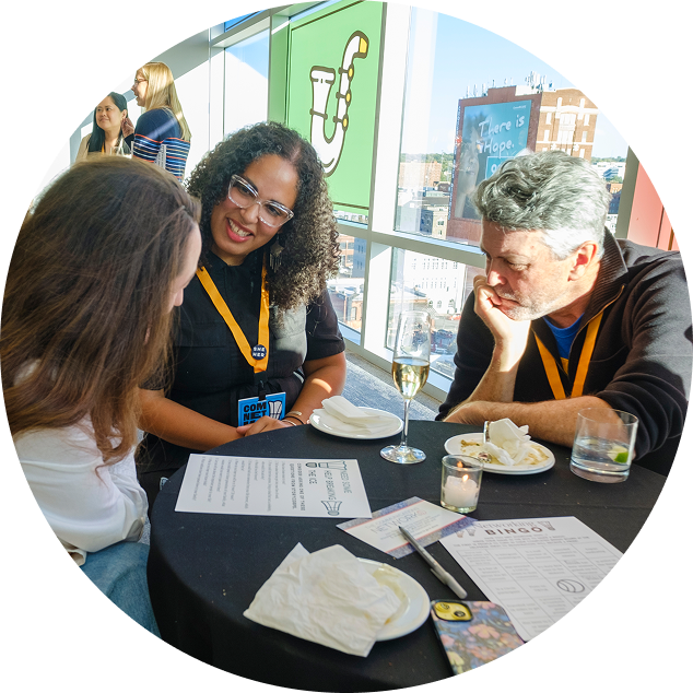 Three people sitting at a round table in a bright room, engaged in conversation, with food and drinks on the table.