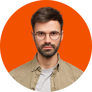 Portrait of a man with glasses and a beard, wearing a beige jacket over a gray shirt, against an orange background.