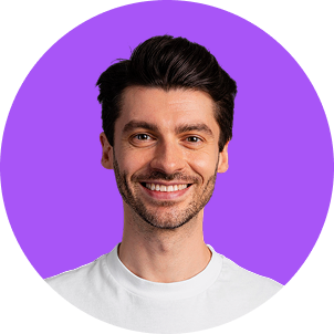 A smiling man with dark hair and a beard wearing a white shirt against a purple background.