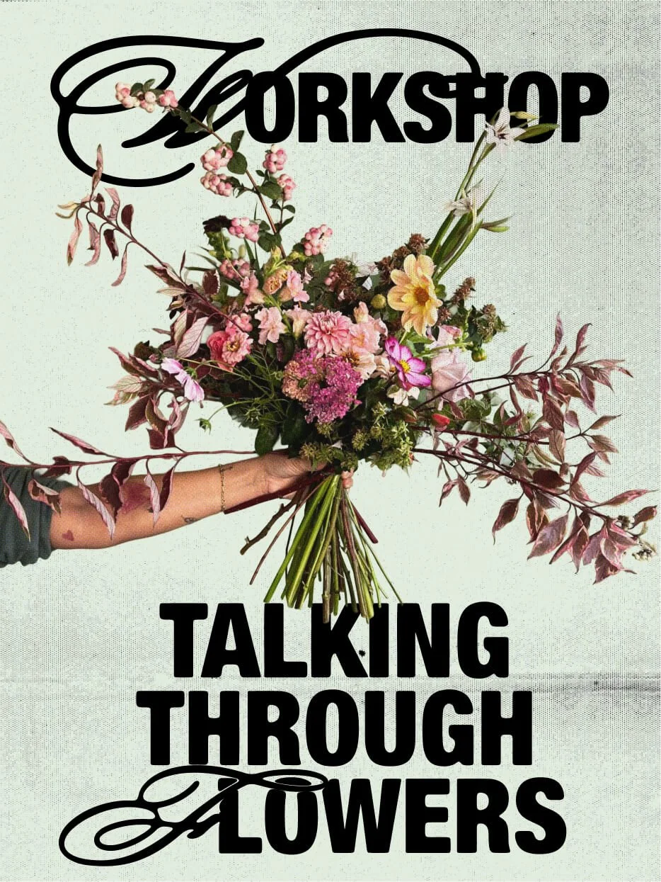 A person holds a bouquet of pink, yellow, and purple flowers with green foliage in front of a wall with the word 'Workshop' and the phrase 'Talking Through Flowers' written. The background is light-colored.
