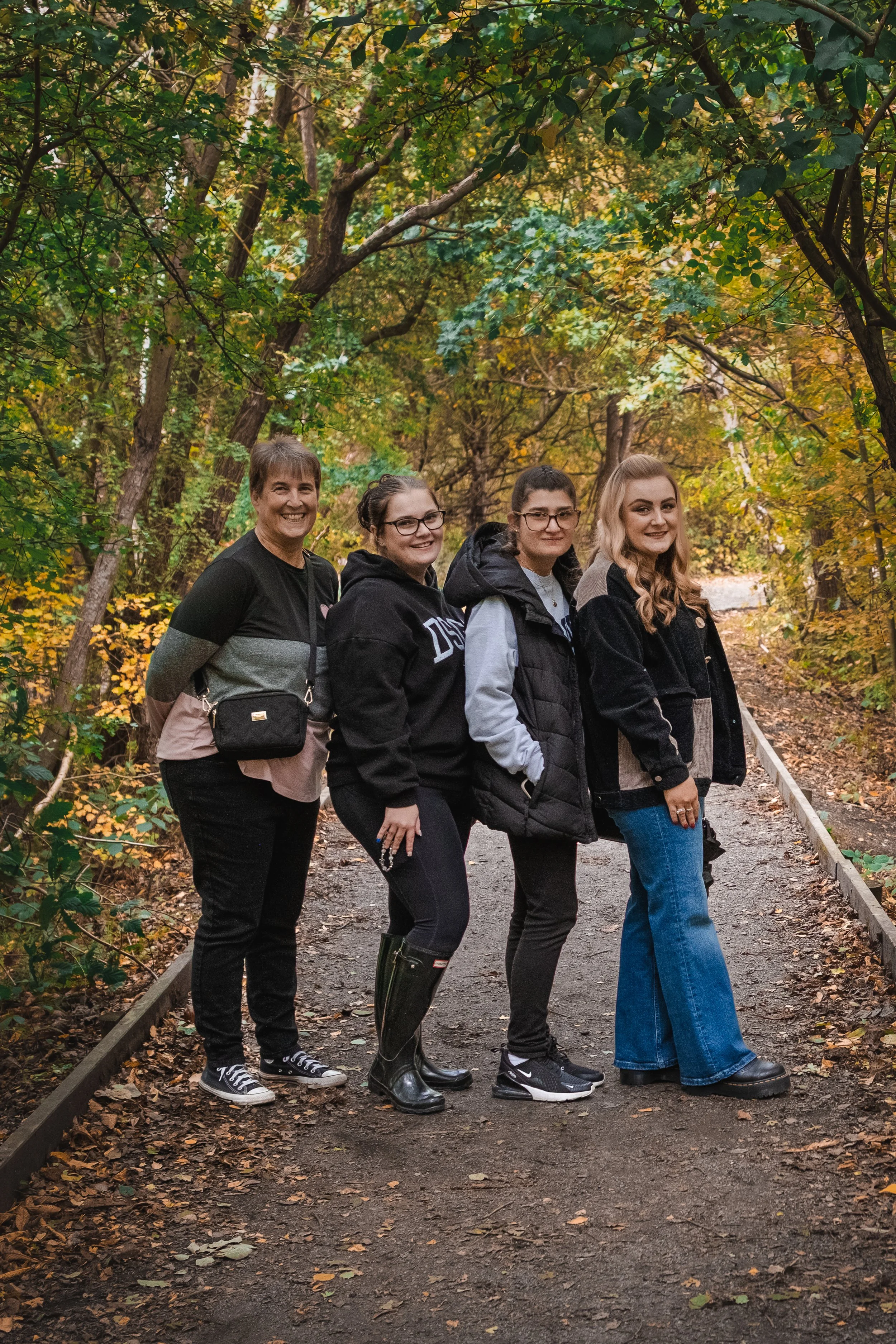 Four women walking on a forest trail during autumn, surrounded by colorful fall foliage.