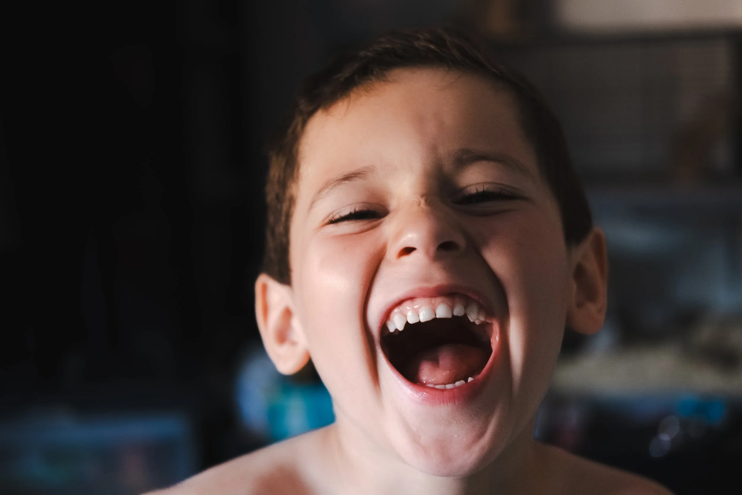 A young boy laughing widely with his mouth open, showing his teeth and joyful expression.