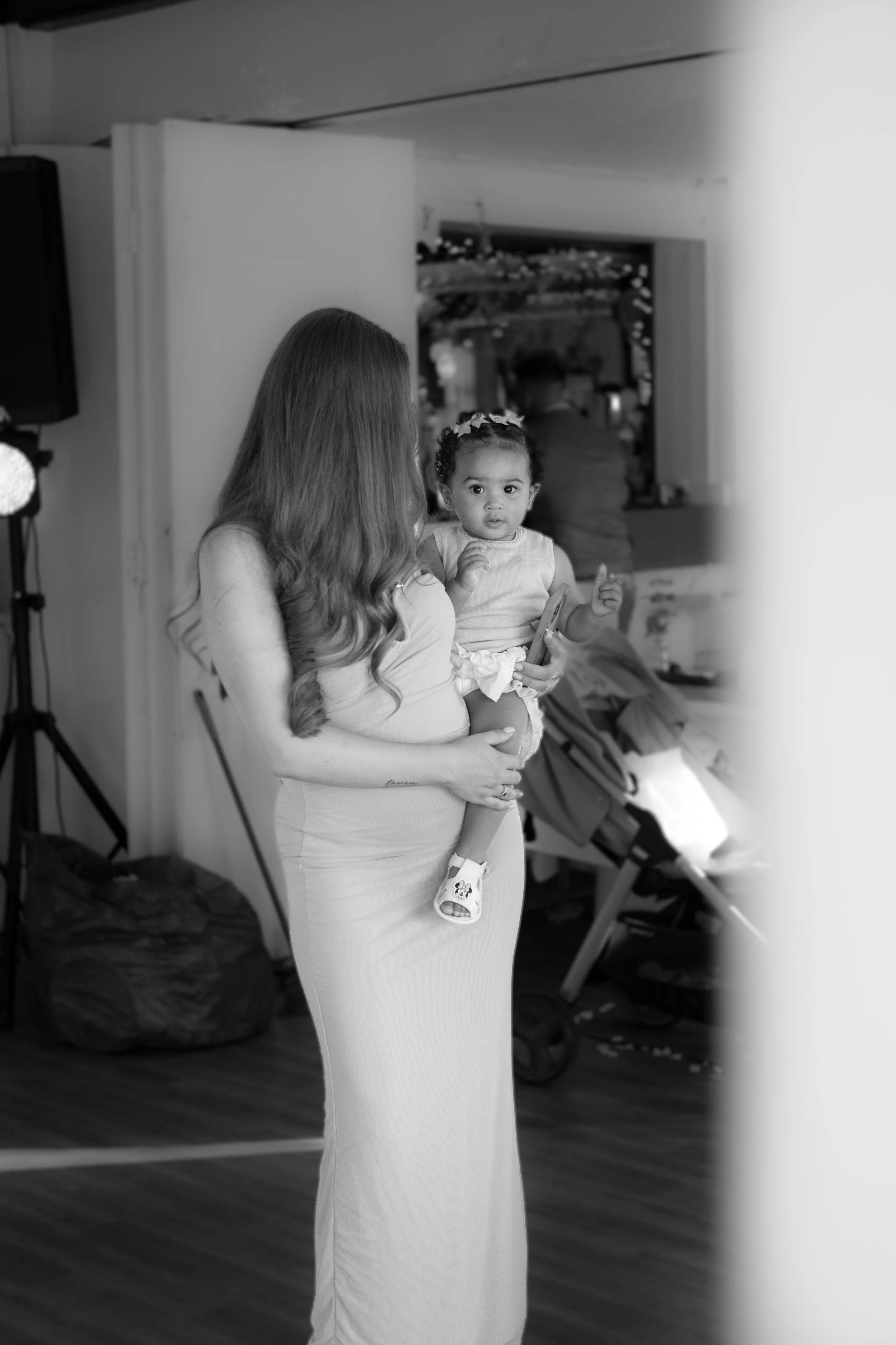 A woman holding a young girl in a room with a stroller and a light stand in the background.