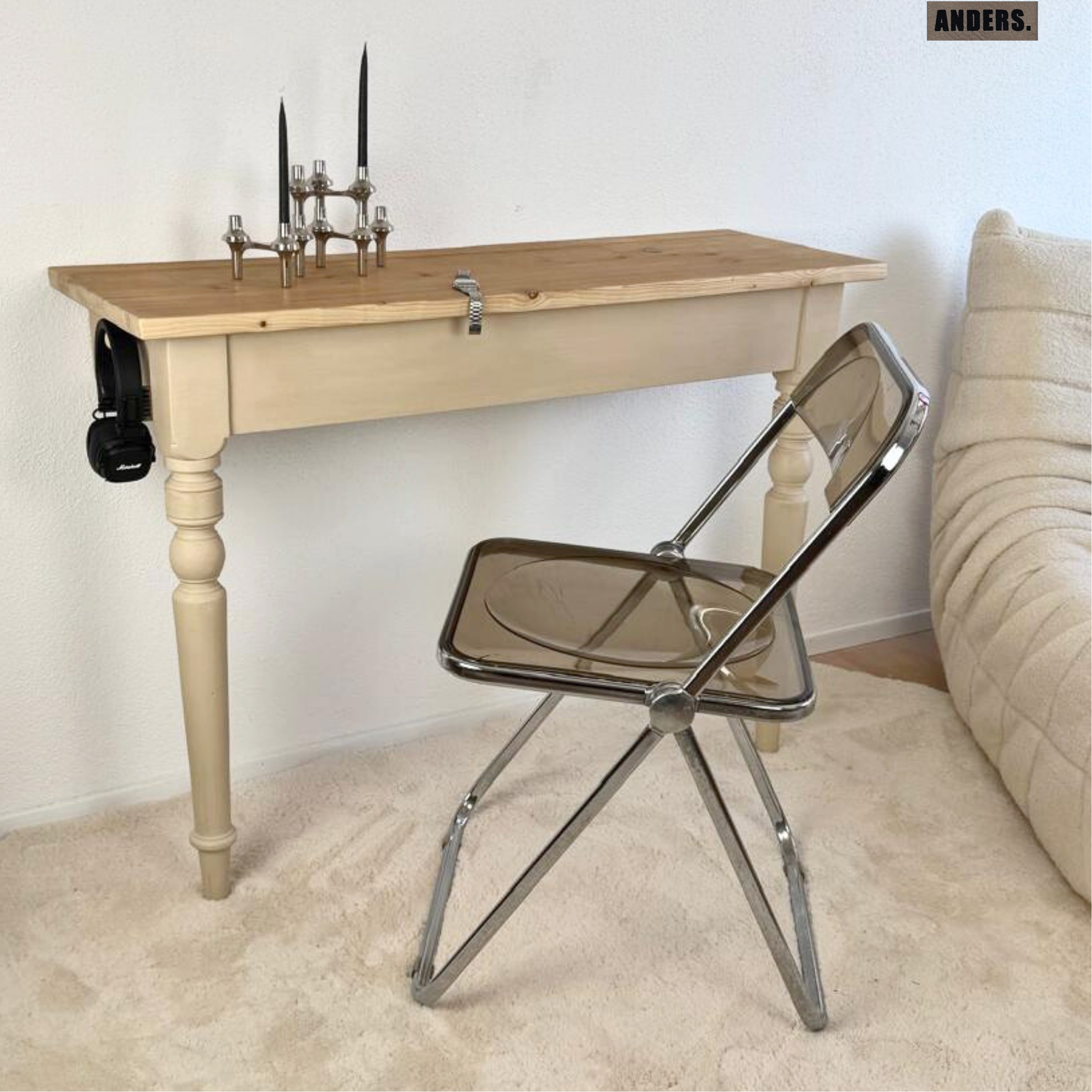 Ein Holztablett mit Kerzen auf einem weißen Tisch und einem transparenten Klappstuhl im Raum.