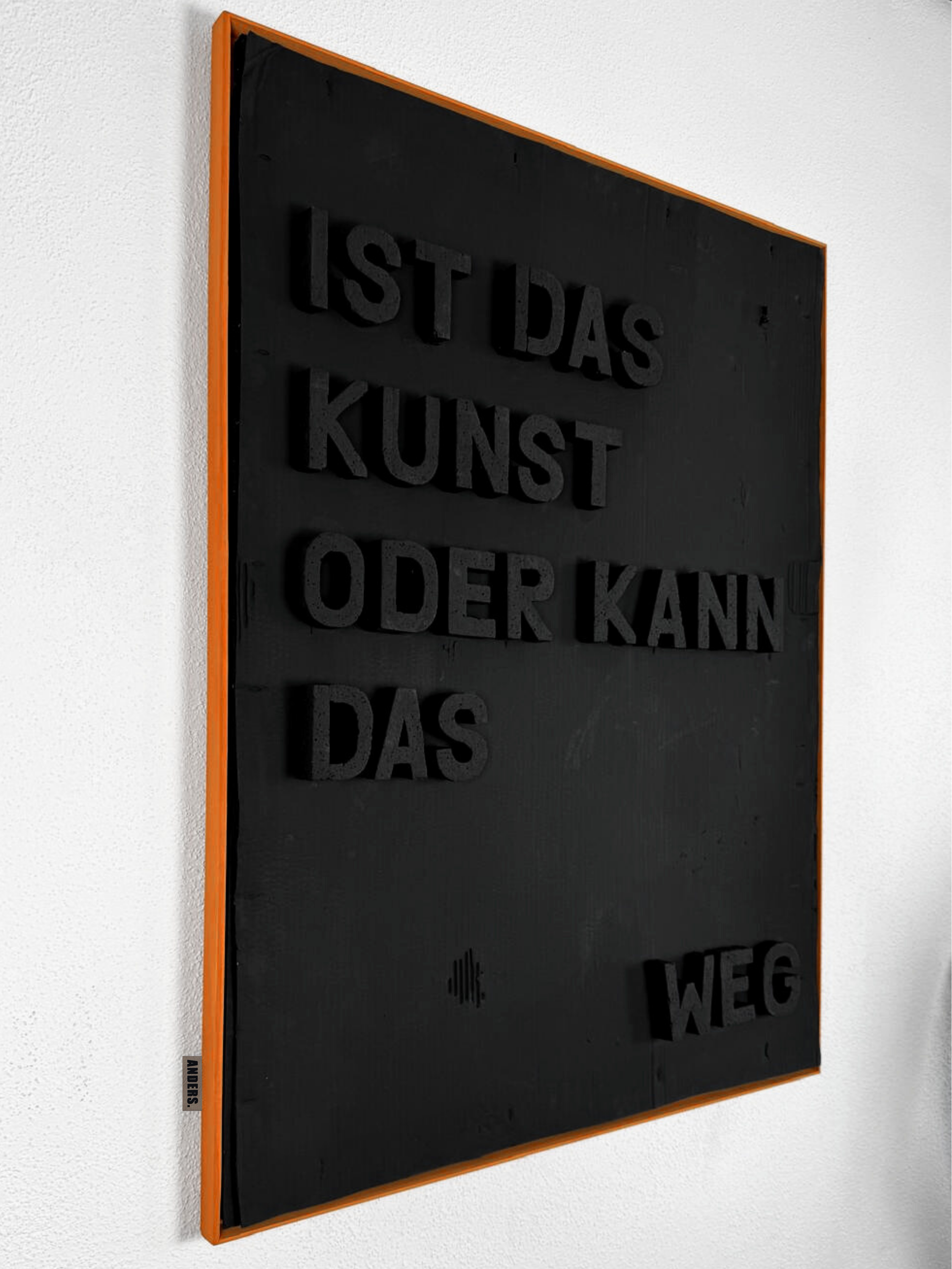 Schwarze Tafel mit deutschem Text in 3D-Schrift, orange Rahmen, an weißer Wand.