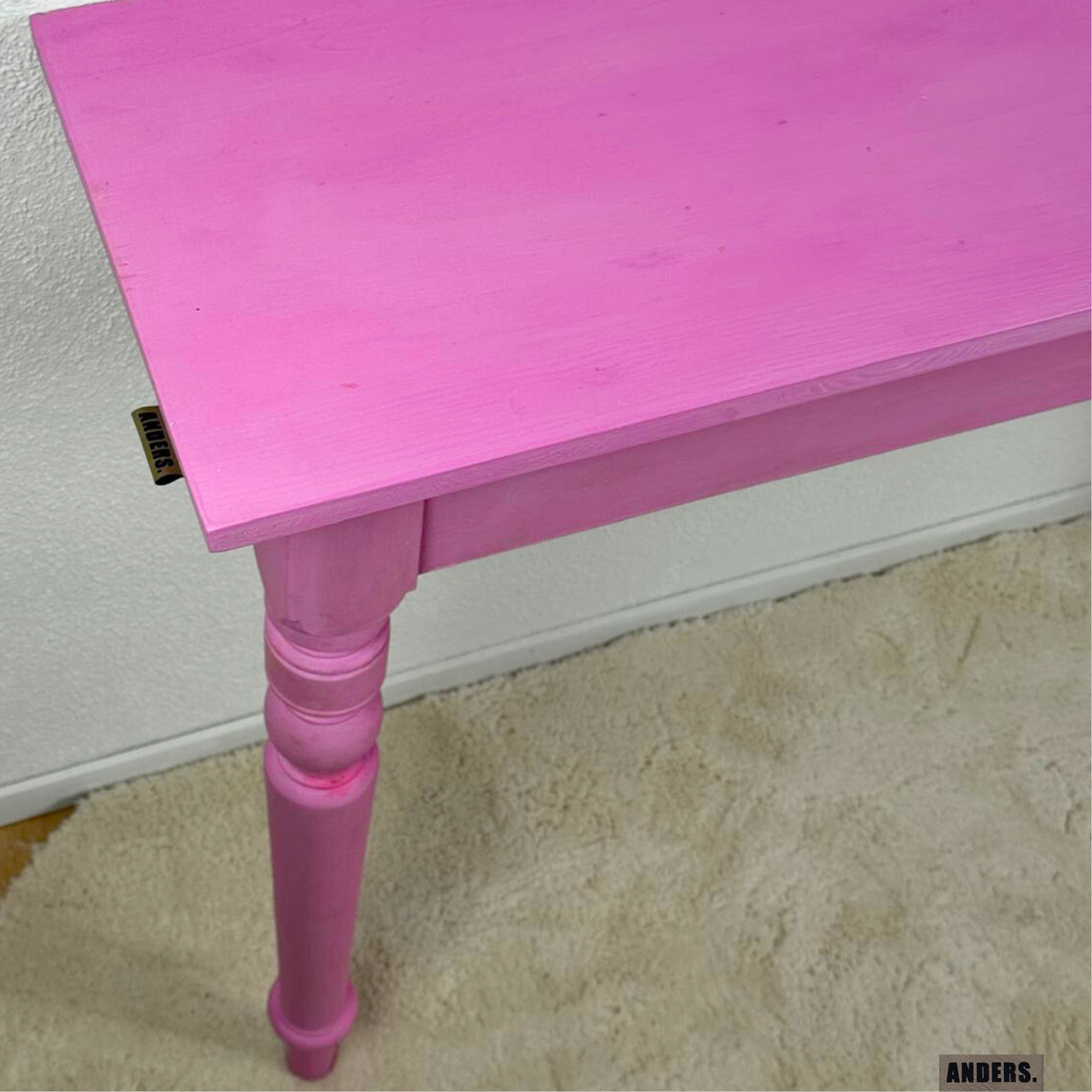 Ein pinkfarbener Holztisch mit gedrechseltem Bein, steht auf einem Teppichboden.