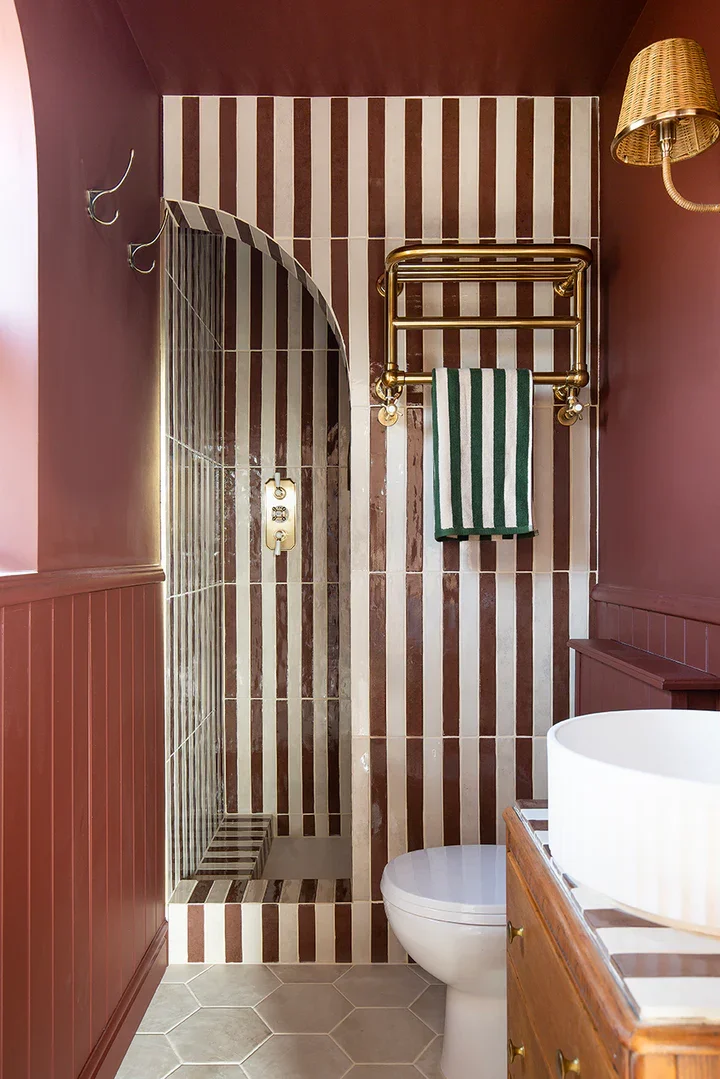 Striped terracotta and white tiled shower with arched opening and brass heated towel rail