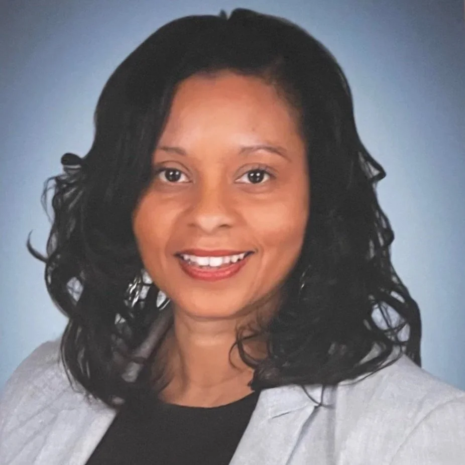 Portrait of a woman with long dark hair, wearing earrings, smiling at the camera.