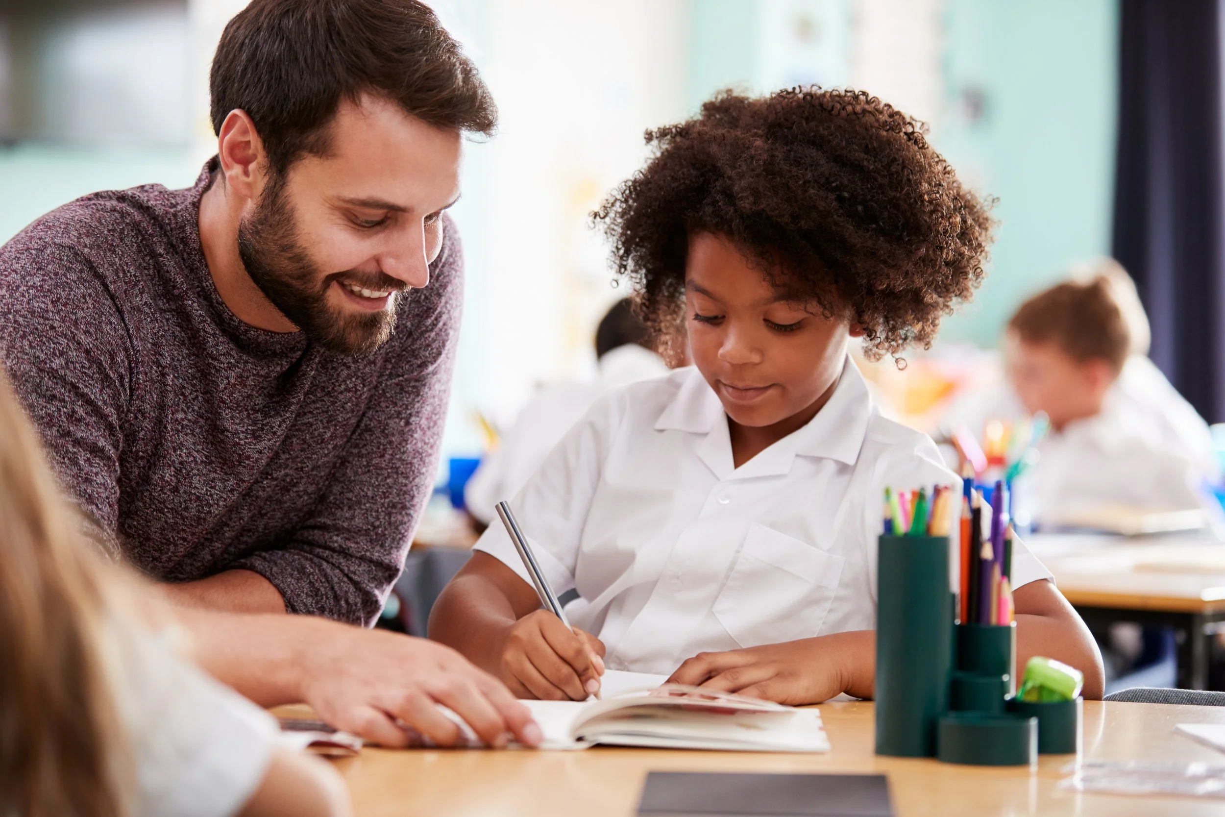 A teacher helping a young girl with her work at a school desk in a classroom.